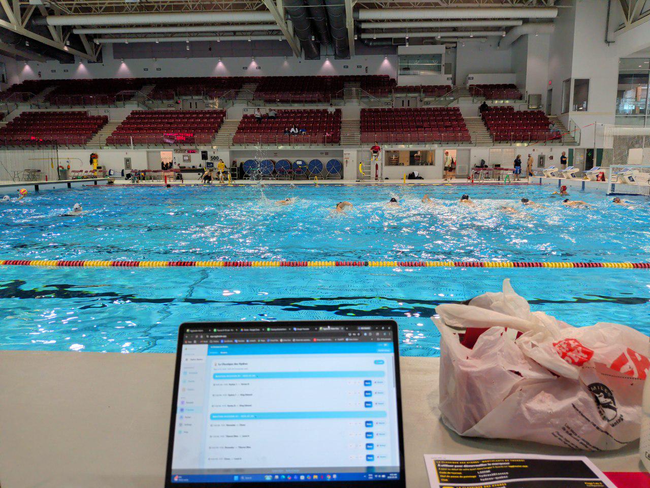 Pool deck at PEPS Laval — laptop with Eggbeater open, water polo match in progress